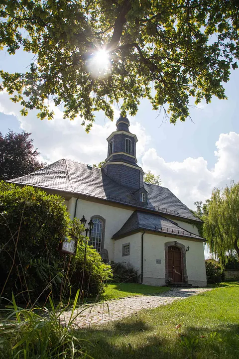 Evangelische Kirche "St. Georg & St. Martin" in Griesbach im Sommerlicht, idyllisch gelegen unter einem Baum mit Sonnenstrahlen im Vordergrund.