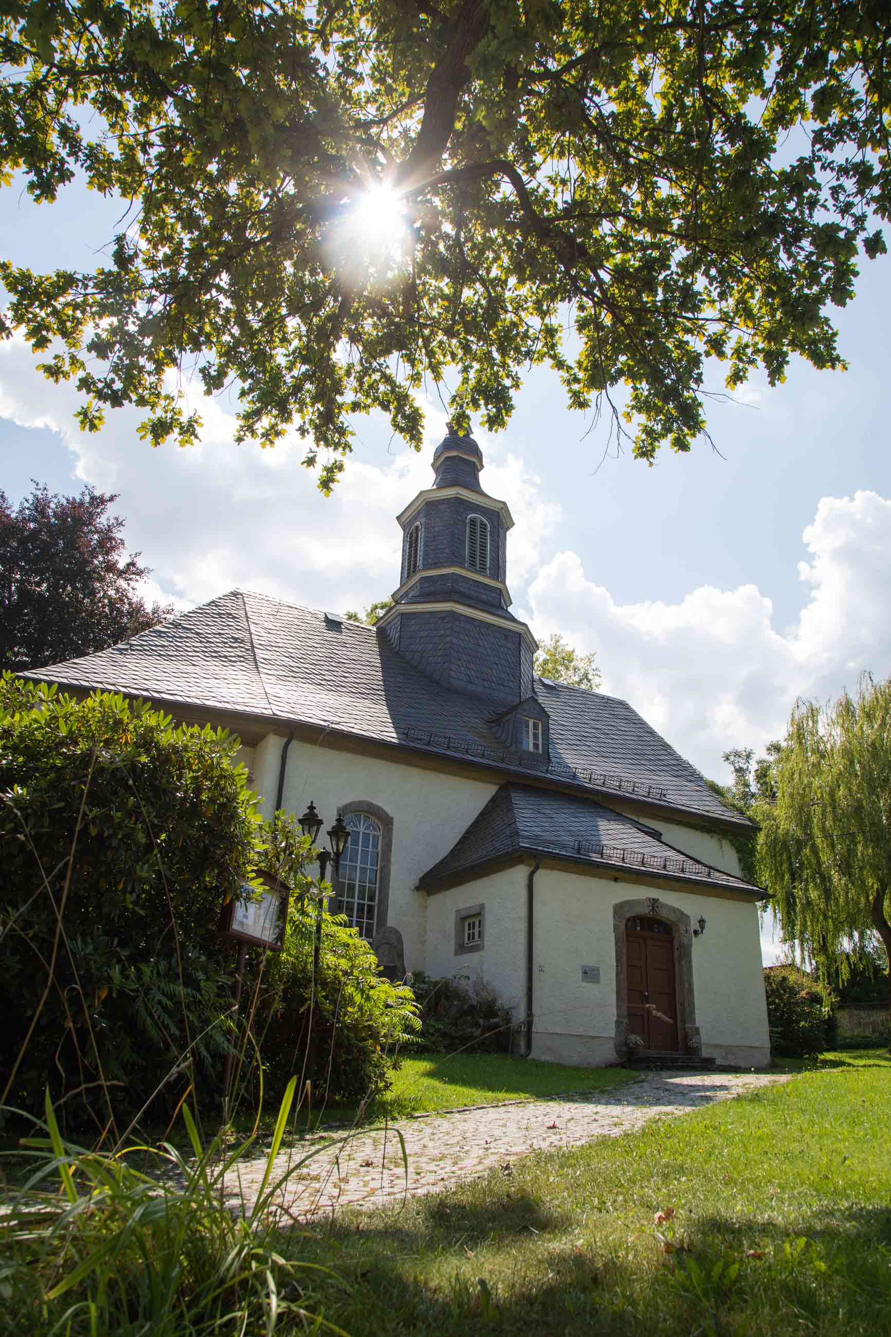 Evangelische Kirche "St. Georg & St. Martin" in Griesbach im Sommerlicht, idyllisch gelegen unter einem Baum mit Sonnenstrahlen im Vordergrund.
