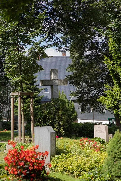 Blick auf das steinerne Kreuz auf dem Friedhof in Neustädtel, sommerliche Lichtstimmung, im Vordergrund zwei Grabsteine zu sehen