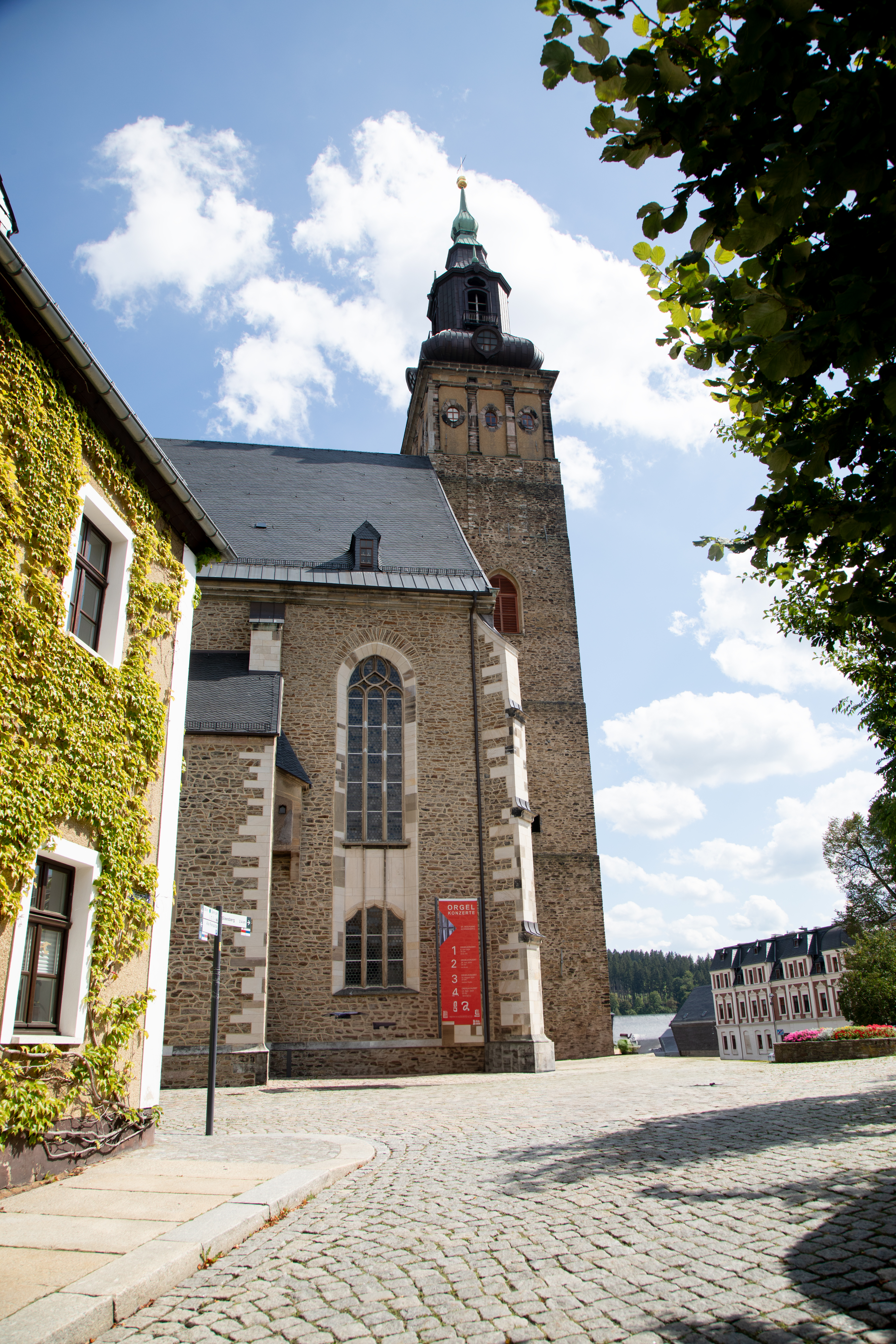 St. Wolfgangskirche in Schneeberg mit markantem Turm und historischer Fassade, Blick über den Kirchplatz an einem sonnigen Tag