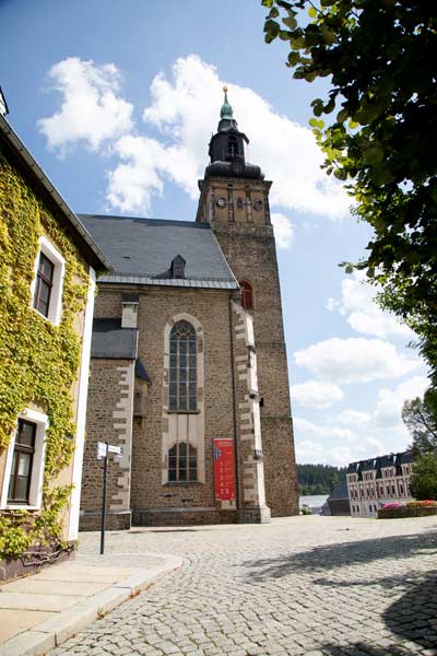 Steinerner Kirchturm und Kirchenschiff auf Kopfsteinpflasterstraße.